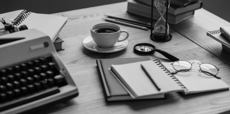 A desk with a typewriter, cup and saucer, notebooks, pen, glasses and books