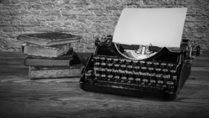 A typewriter with a sheet of paper loaded, next to a stack of books