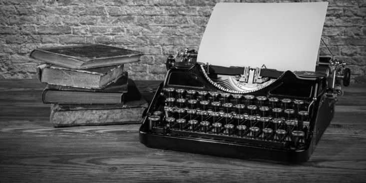 A typewriter with a sheet of paper loaded, next to a stack of books